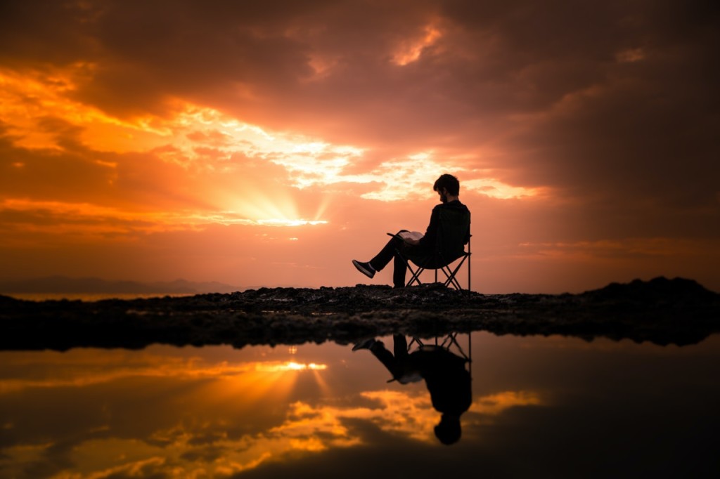 Nell'immagine un uomo legge su di una sdraio in riva al mare al tramonto - Smart Marketing