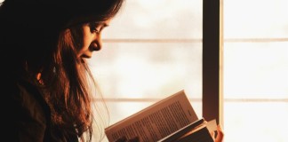 Nell'immagine una donna legge un libro vicino ad una finestra - Smart Marketing