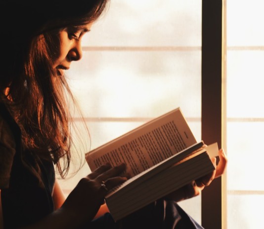 Nell'immagine una donna legge un libro vicino ad una finestra - Smart Marketing