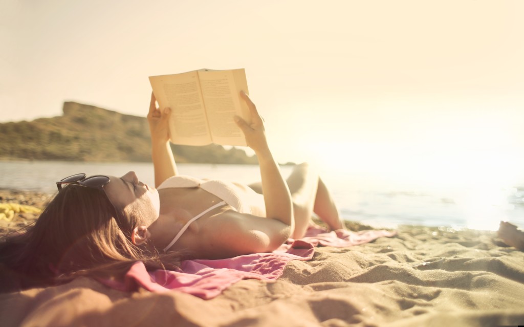 Nell'immagine una donna sdraita in spiaggia legge un libro - Smart Marketing