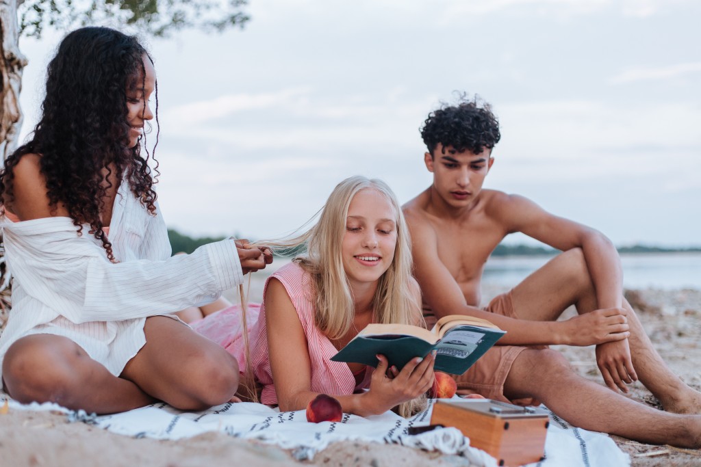 Nell'immgine tre ragazzi sulla spiaggia stanno leggendo - Smart Marketing