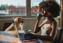 Nell'immagine una ragazza lavora al computer, in pigiama, sorseggiando caffè in compagnia di un cane - Smart Marketing
