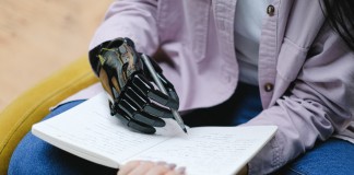 Nell'immagine un uomo con una mano bionica scrive su di un quaderno - Smart Marketing