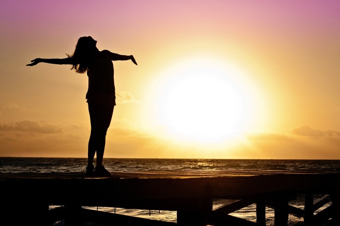 Nella foto una ragazza con le braccia aperte sullo sfondo di un tramonto - Samart Marketing