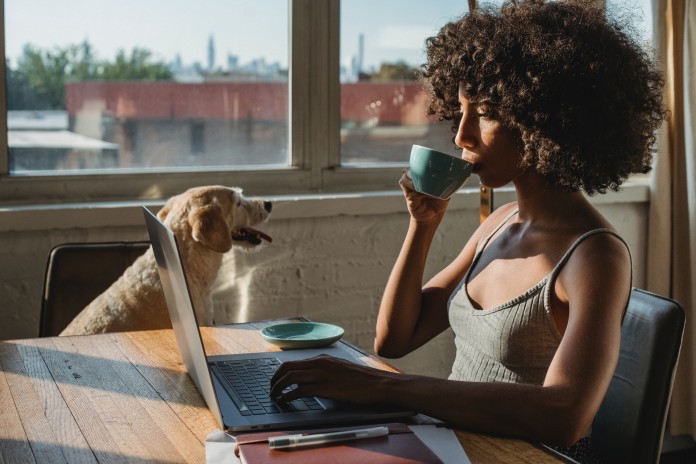 Nell'immagine una ragazza lavora al computer, in pigiama, sorseggiando caffè in compagnia di un cane - Smart Marketing