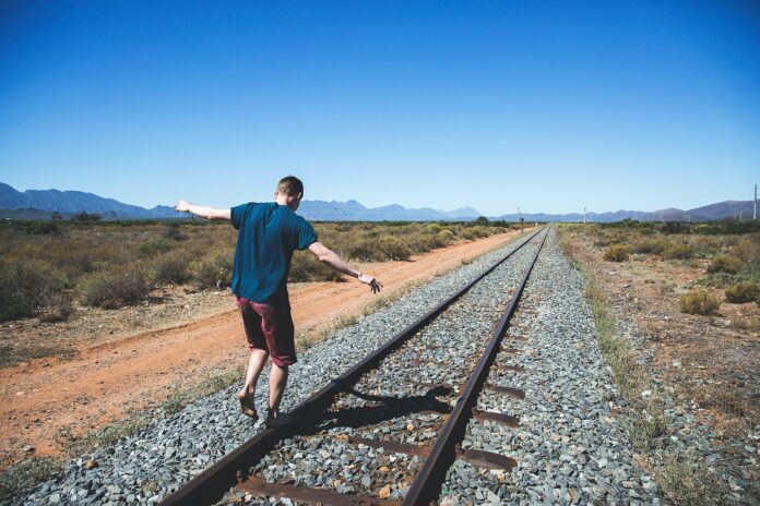 Nell'immagine un ragazzo cammina in equilibrio sui binari del treno - Smart Marketing